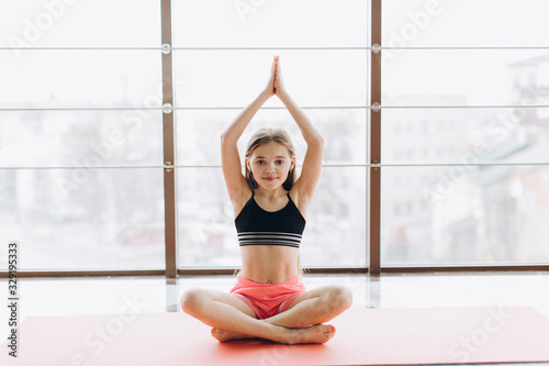 Charming little girl is smiling while doing yoga in fitness hall