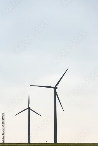 Two wind farms and a human silhouette showing the scale of these objects. All on the background of blue sky and green field. © mckornik