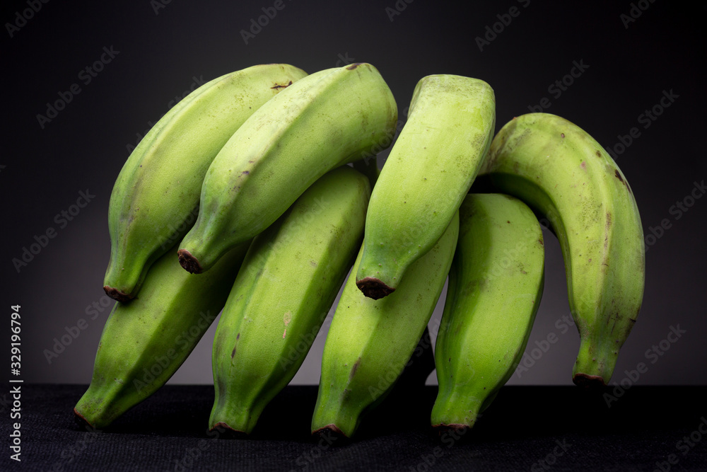 Brightly lit vibrant green bundle of bananas on a black surface with dark grey studio background