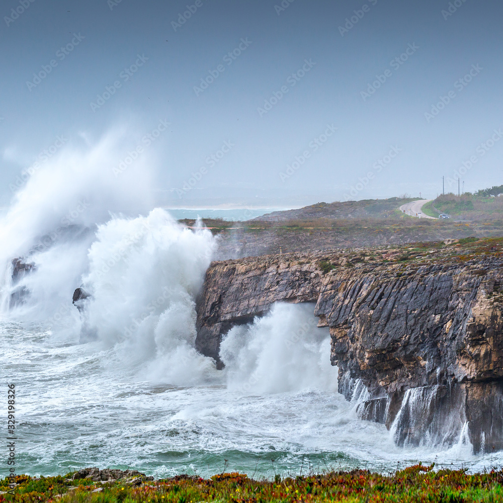 A huge ocean waves breaking on the coastal cliffs in at the cloudy stormy day. Breathtaking romantic seascape of ocean coastline.