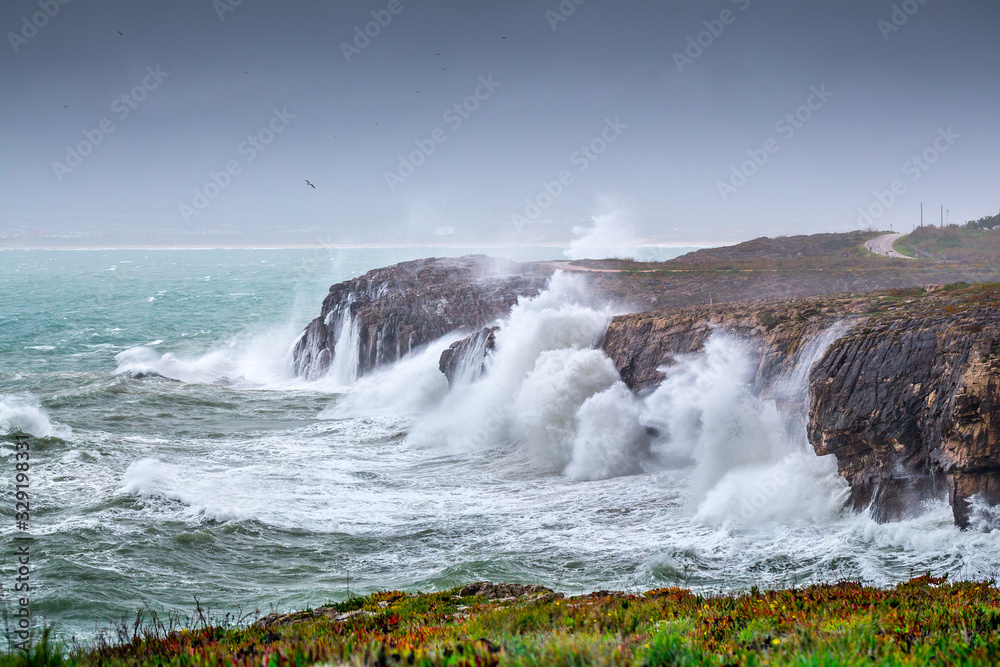 A huge ocean waves breaking on the coastal cliffs in at the cloudy stormy day. Breathtaking romantic seascape of ocean coastline.