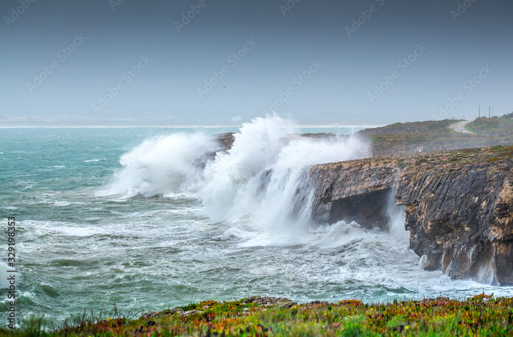 A huge ocean waves breaking on the coastal cliffs in at the cloudy stormy day. Breathtaking romantic seascape of ocean coastline.