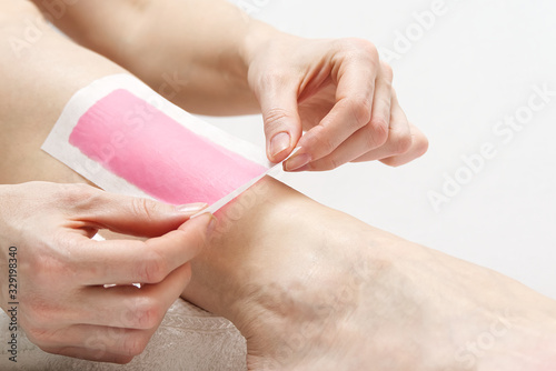 Woman using pink wax strips. Beautiful woman doing depilation for her legs with waxing  isolated on white