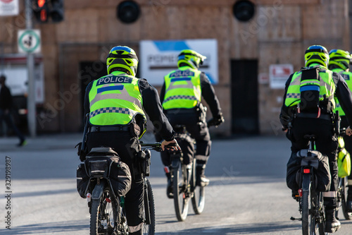 Four cyclist police officers are seen from the rear, wearing high visibility vest and safety helmet, uniformed on duty law enforcement at climate rally