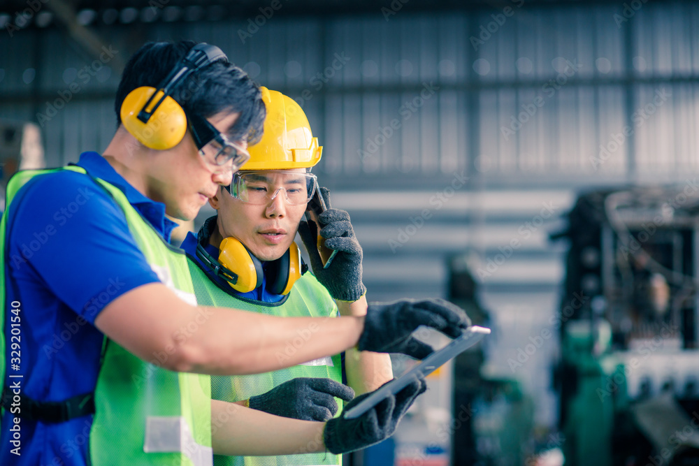 Two asian maintenance engineers discuss inspect relay checking information and protection system on a tablet computer in a factory. They work a heavy industry manufacturing factory. Two asian maintenance engineers discuss inspect relay checking information and protection system on a tablet computer in a factory. They work a heavy industry manufacturing factory.