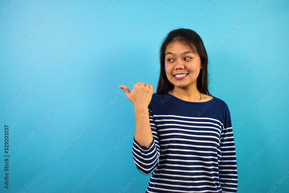 Portrait of Young beautiful asian women with blue isolated background, points away on copy space, helps pick best choice, recommends product. Portrait of Young beautiful asian women with blue isolated background, points away on copy space, helps pick best choice, recommends product.