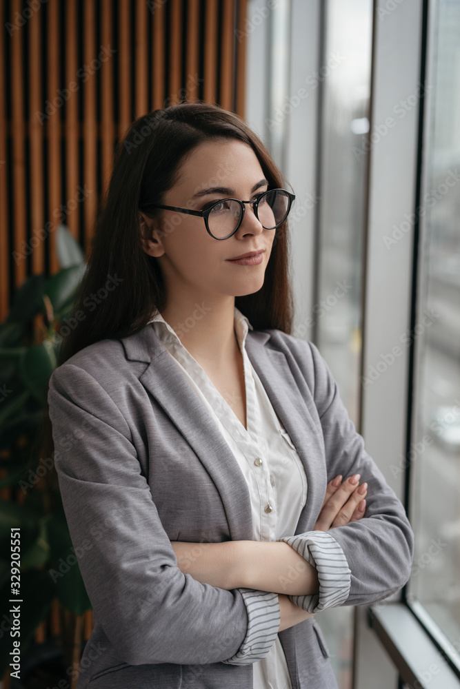 Pensive businesswoman with arms crossed planning start up in office . Portrait of young manager in formal clothes and stylish eyeglasses thinking near window, brainstorming. Successful business Pensive businesswoman with arms crossed planning start up in office . Portrait of young manager in formal clothes and stylish eyeglasses thinking near window, brainstorming. Successful business