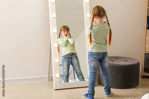 Surprised little girl looking in mirror at home