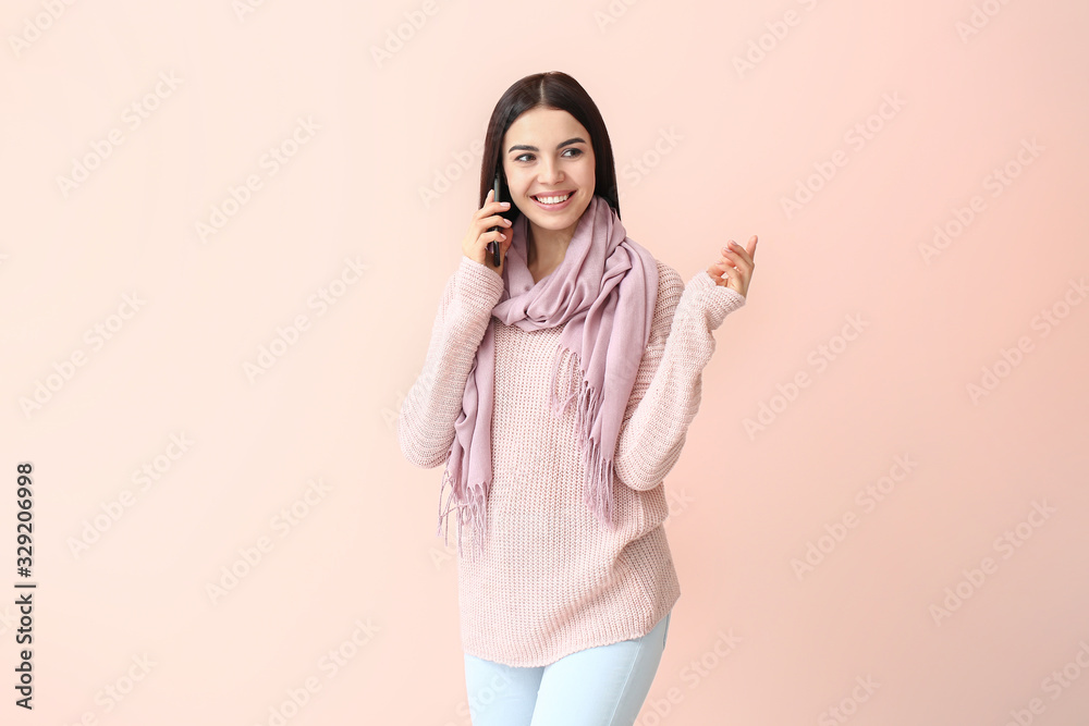 Beautiful young woman in warm sweater talking by phone on color background Beautiful young woman in warm sweater talking by phone on color background