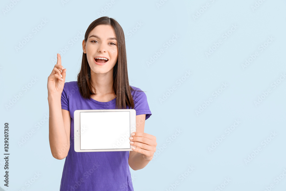 Young woman with tablet computer and raised index finger on light background