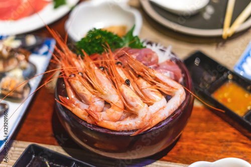 brown wooden bowl of prawns or shrimps laid elegantly with tunas and side dressing of vegetables, laid on the table with sauces, spices and sashimi dishes round it within a japanese sushi restaurant