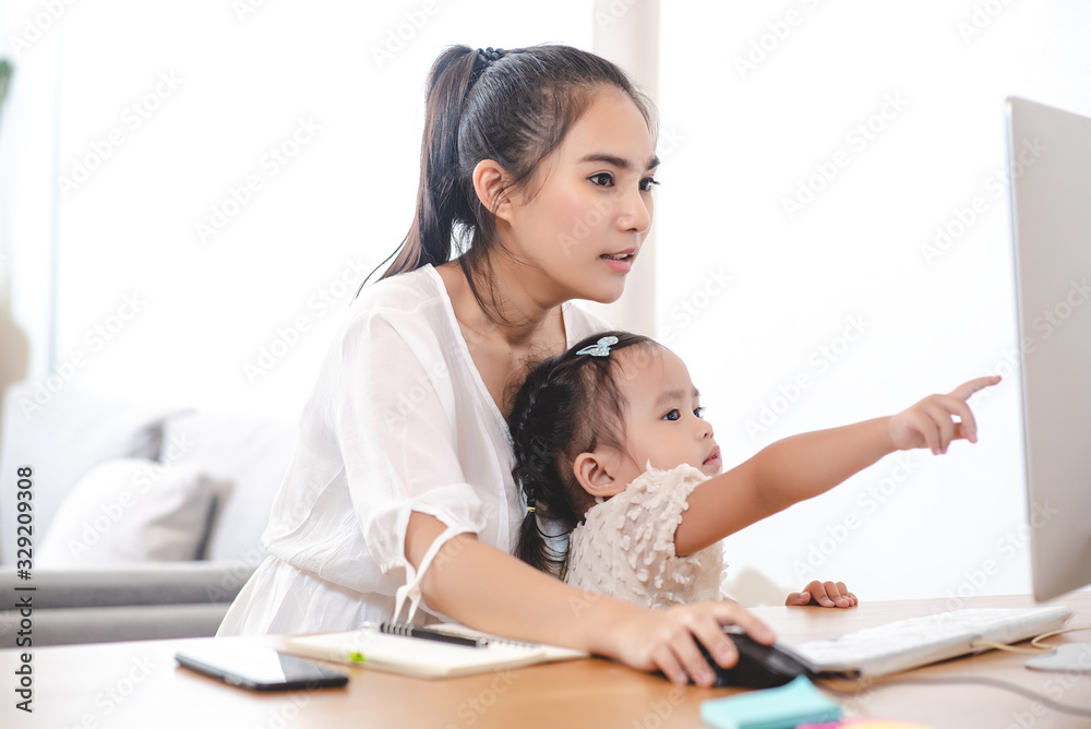Asian mother watching her daughter who is learning to use the computer. Mom and kids, education, family relationship, child care, technology for children concept. Asian mother watching her daughter who is learning to use the computer. Mom and kids, education, family relationship, child care, technology for children concept.