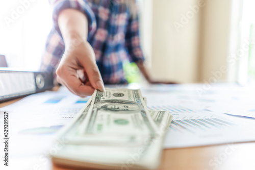 close up of worker picking up pile of cash money bills stack on the wooden table, laying on top of work documentation of the business with folder files nest to it, representing business and payment