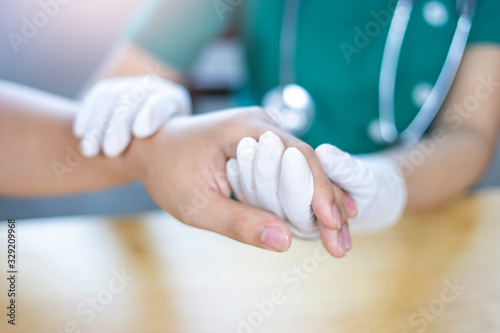close up a female doctor holding a patients hand, representing comfort, warmth and closure, in an medical office room with paper documents, computer laptop and smart tablet device on the wooden table