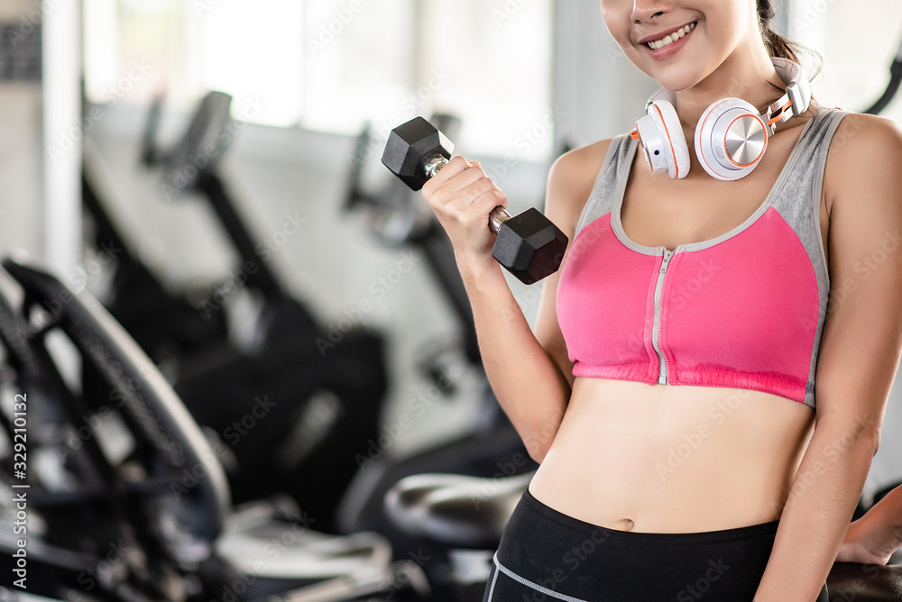 Healthy Asian woman lifting dumbbells in the gym with smile and fresh face. Exercise, workout, muscle training, weight lifting, weight loss, heart rate practice and diet concept. Healthy Asian woman lifting dumbbells in the gym with smile and fresh face. Exercise, workout, muscle training, weight lifting, weight loss, heart rate practice and diet concept.
