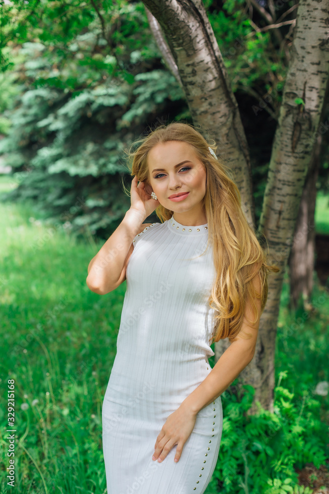 Portrait of a charming blond woman wearing beautiful white dress standing next to rowan tree. Portrait of a charming blond woman wearing beautiful white dress standing next to rowan tree.