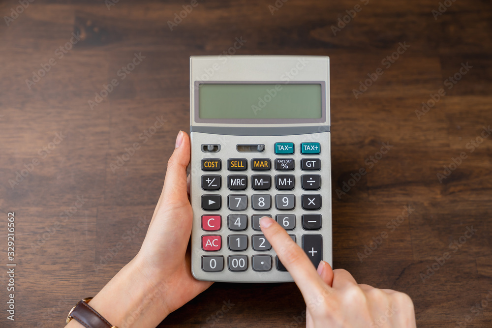 Close-up of hand holding calculator on wood table. Close-up of hand holding calculator on wood table.