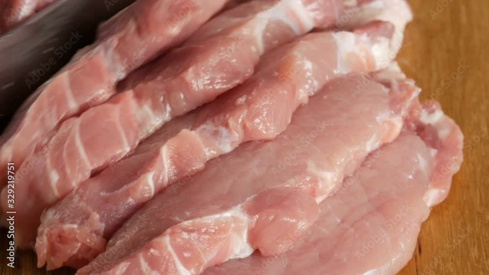 Close up view of female hands of a cook cut fresh pieces of pork bacon meat on a wooden kitchen board in a rustic style with a large kitchen knife. Close up view of female hands of a cook cut fresh pieces of pork bacon meat on a wooden kitchen board in a rustic style with a large kitchen knife.