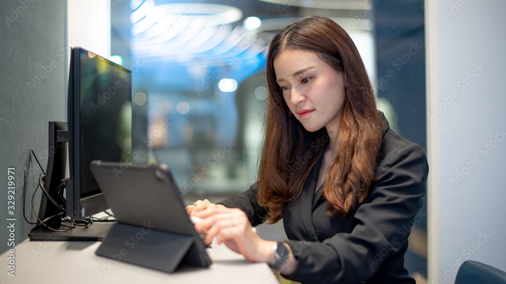 Working woman concept. Attractive young Asian businesswoman using digital tablet and computer working in modern office. Confident Female entrepreneur smiling at workplace. Work smart with technology.