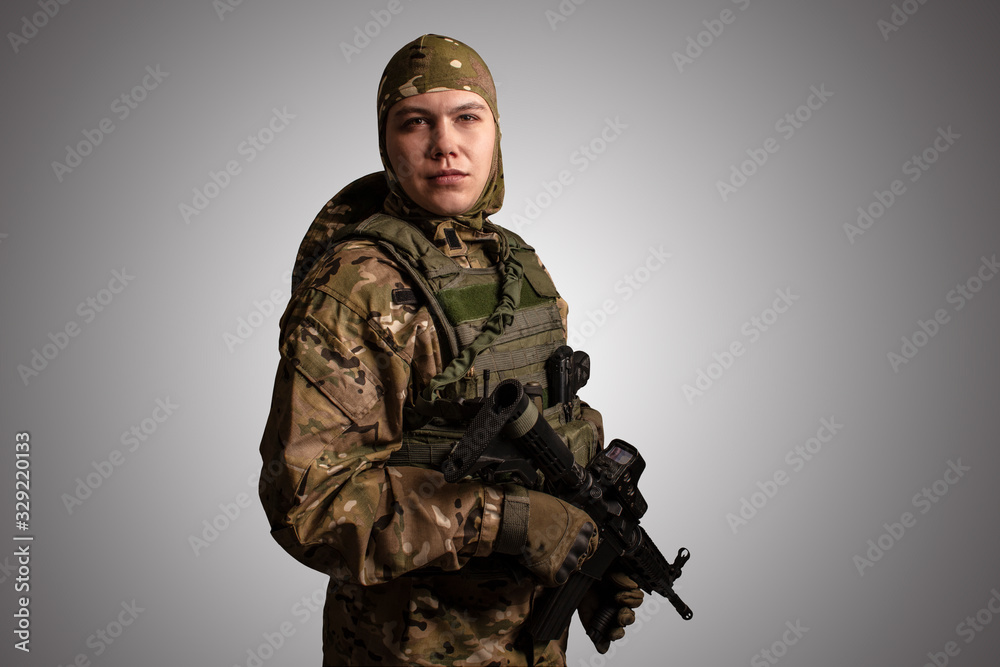 Portrait of soldier in military camouflage uniform protected with helmet, body armour, holding machine gun desaturated on a gray background. Portrait of soldier in military camouflage uniform protected with helmet, body armour, holding machine gun desaturated on a gray background.