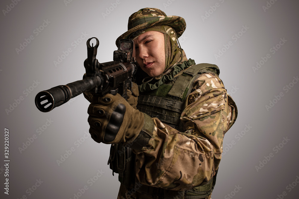 Portrait of soldier in military camouflage uniform protected with helmet, body armour, holding machine gun desaturated on a gray background. Portrait of soldier in military camouflage uniform protected with helmet, body armour, holding machine gun desaturated on a gray background.