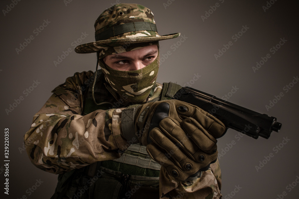Portrait of soldier in military camouflage uniform protected with helmet, body armour, Holding machine gun desaturated on a gray background. Portrait of soldier in military camouflage uniform protected with helmet, body armour, Holding machine gun desaturated on a gray background.