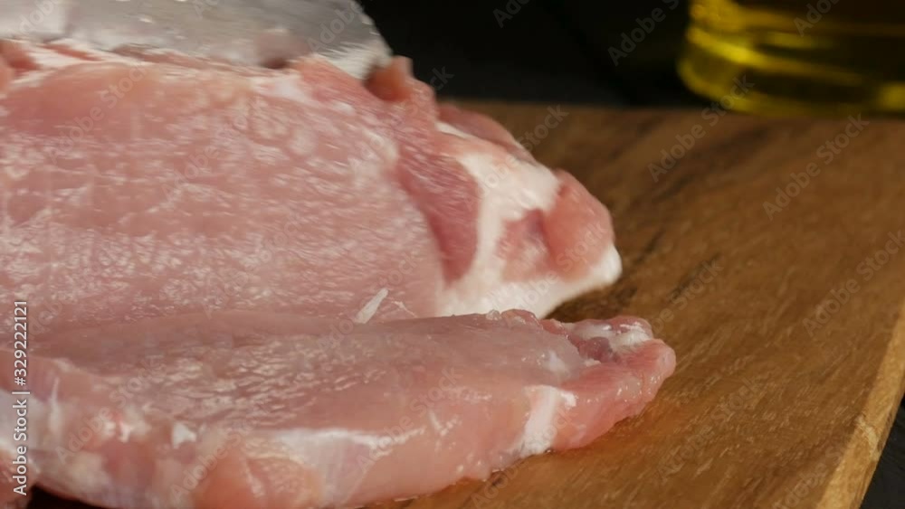 Close up view of female hands of a cook cut fresh pieces of pork bacon meat on a wooden kitchen board in a rustic style with a large kitchen knife. Close up view of female hands of a cook cut fresh pieces of pork bacon meat on a wooden kitchen board in a rustic style with a large kitchen knife.