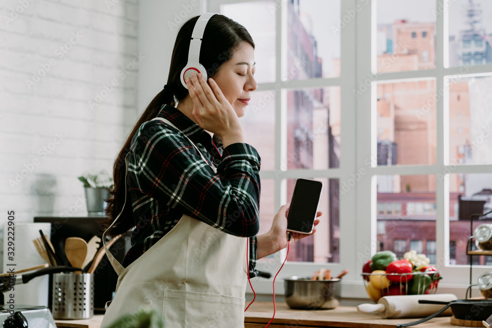 Φωτογραφία Beautiful young girl listening to music with headphones while standing at kitchen counter