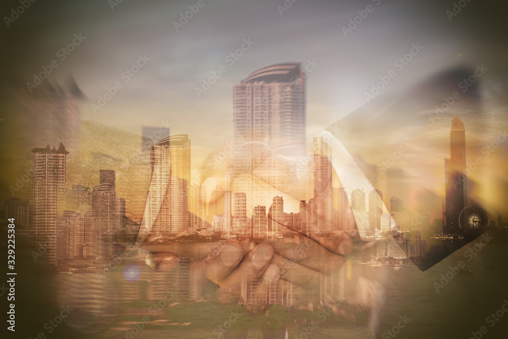 The hand of a business person is hands shaking against the big city in the background.Double Exposure Image.