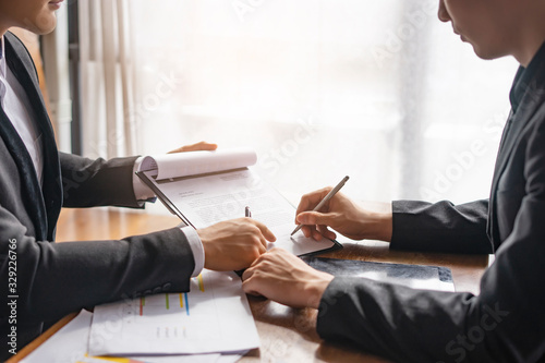 asian businessmen having a meeting discussing partnership signing contract of agreement on clipboard with tablet device and papers of statistics lying on the table, sitting across from each together photo