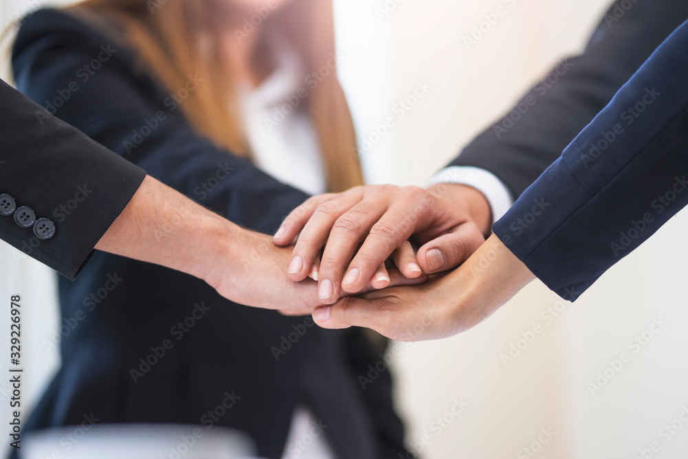 asian businessmen and businesswomen putting hands together piling on top of one another representing teamwork, community, help and support within the business or company within an office environment asian businessmen and businesswomen putting hands together piling on top of one another representing teamwork, community, help and support within the business or company within an office environment