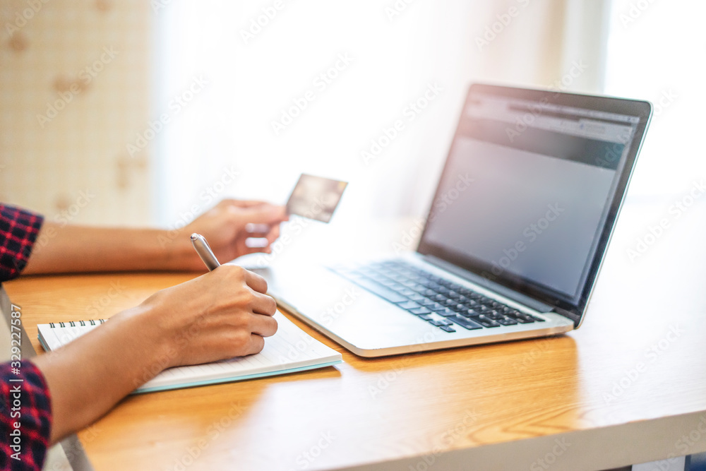 Fototapeta premium closeup of hands with a laptop computer, using it to browsing through ecommerce doing online shopping and paying for a product, using credit card and entering billing information on the purchasing..