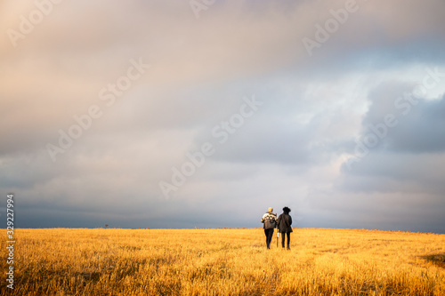 two adventurers walking in amazing endless fields with beautiful blue sky and lovely white clouds above their head and enjoying the freedom and peace.