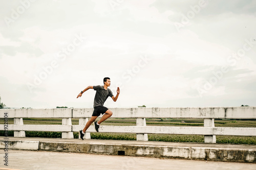 Fotografija asian teenager running along the bridge in sprinting action, exercising or pract