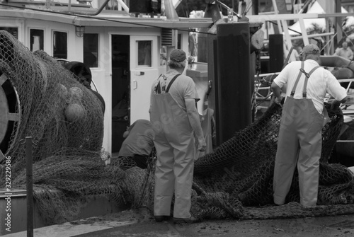 2old fishermen stand beside their boat and repair their fishing net.