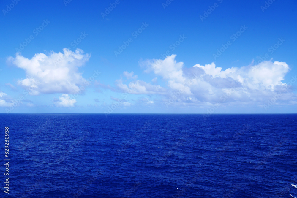 Fototapeta premium Soft white clouds pass over the calm cobalt blue waters of the Caribbean Sea as seen from the deck of a cruise ship.