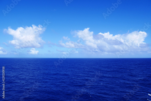 Soft white clouds pass over the calm cobalt blue waters of the Caribbean Sea as seen from the deck of a cruise ship.