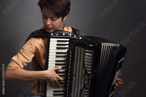 Obraz na płótnie A brunette in a gold shirt, with short haircut, on a light gray background of the Studio. With accordion musician w salonie