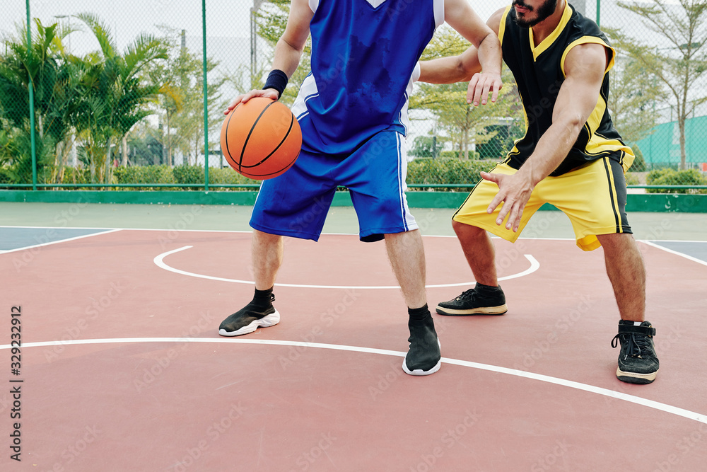Fototapeta premium Cropped image of young men playing basketball on outdoor court