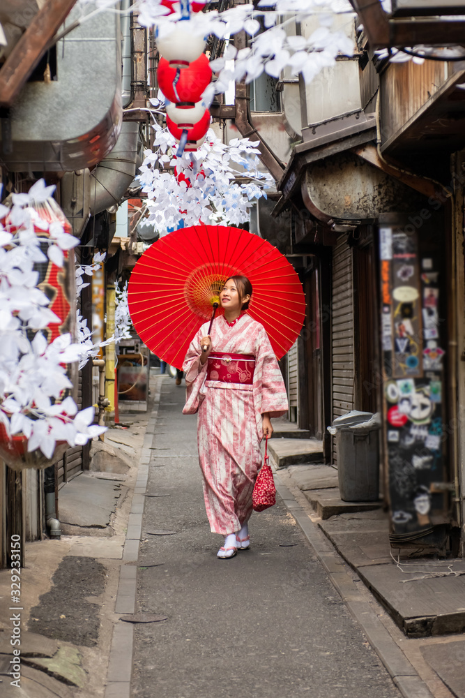 Portrait of Happy young attractive beautiful Asian woman girls wearing pink traditional Japanese kimono dress holding red paper umbrella parasol walking down the street in Tokyo city with smiling face
