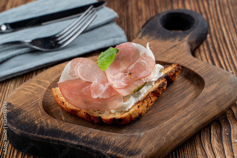 Bruschetta with sliced prosciutto and rich cream cheese on toasted ciabatta on wooden cutting board
