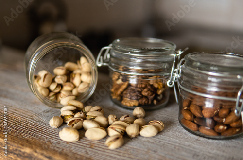 Pistachios scattered on the white vintage table from a jar and with other nuts on background. Pistachio is a healthy vegetarian protein nutritious food. Pistachios on rustic old wood.