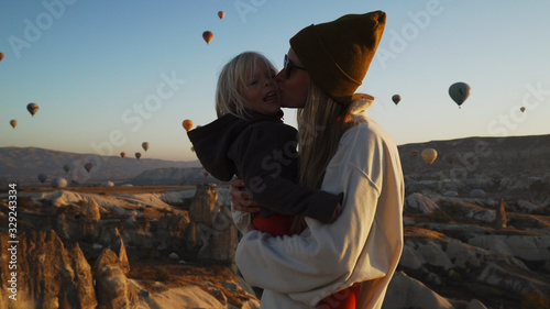 Young blond mother with her kid spinning around in front of air balloons