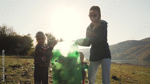 Young mother and her daughters carry a green bag full of trash counter light