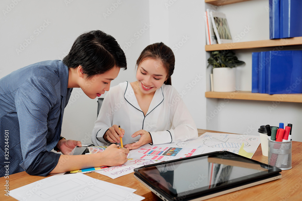 Smiling team of UX and UI designers discussing project details at meeting and choosing color palette