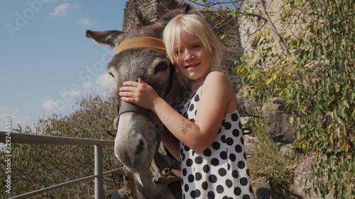 Portrait of little blonde caucasian girl with donkey look at camera