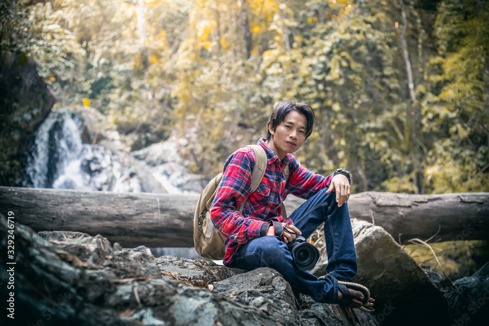 Tourists man sitting and holding camera in forest with waterfall background