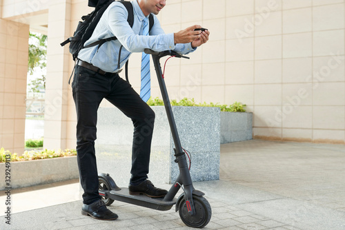 Cropped image of positive entrepreneur checking map application on smartphone before riding electric kick scooter photo