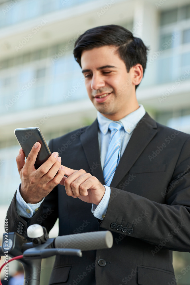 Fototapeta premium Attractive smiling young entrepreneur sending text message to coworker