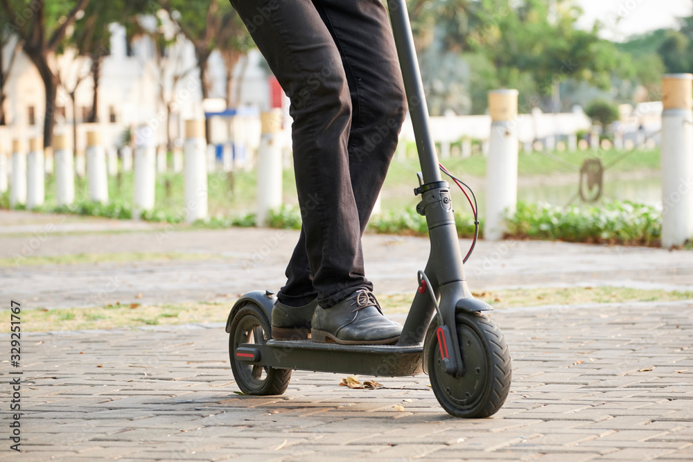 Obraz premium Cropped image of young businessman riding on electric kick scooter in city park and hurrying to work